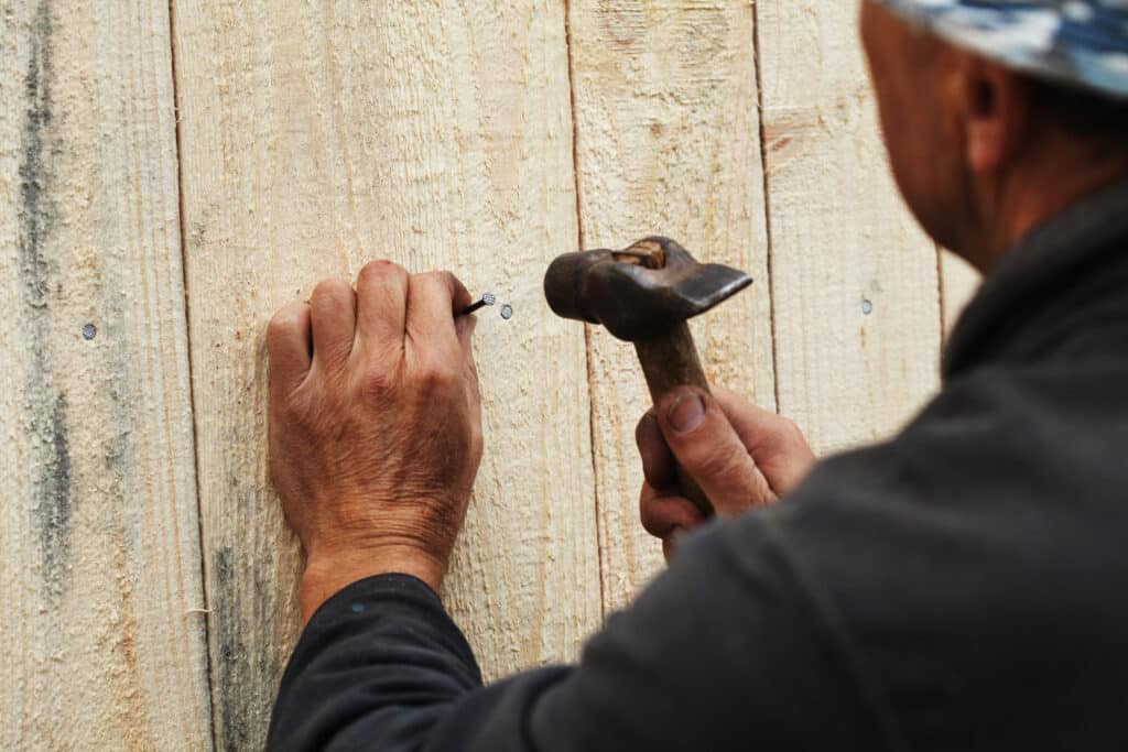 Man fixing wooden plank with a nail. Choosing a Fencing Contractor
