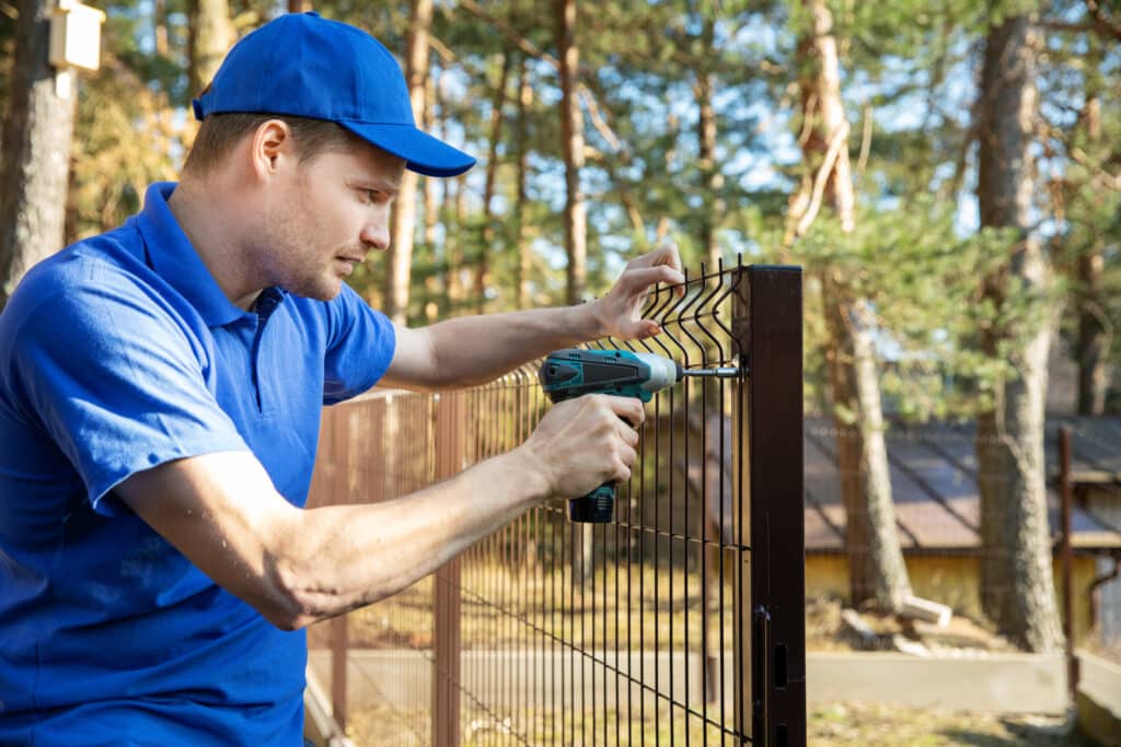 fencing services - worker installing welded metal mesh fence. Choosing a Fencing Contractor